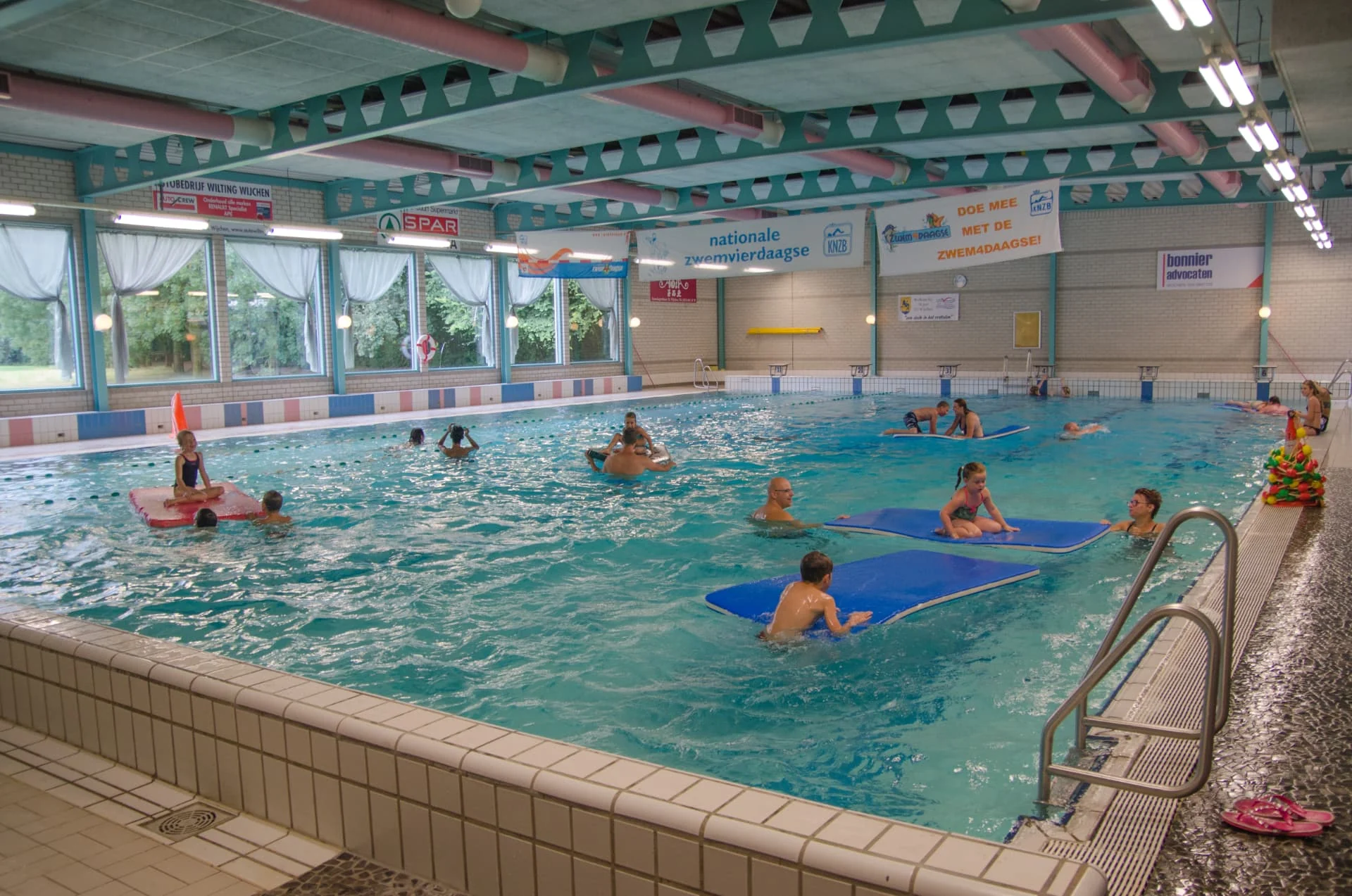 Het wedstrijdbad van Zwembad De Meerval met zwemmers en drijvende matten, onder het plafond van de zwemhal